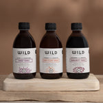 Three amber glass bottles of Wild Dispensary tonics on a wooden board with a brown background.
