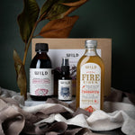A curated gift set including an Immunity Tonic, Fire Cider and Throat Spray arranged on draped fabric in front of a gift box with decorative leaves.