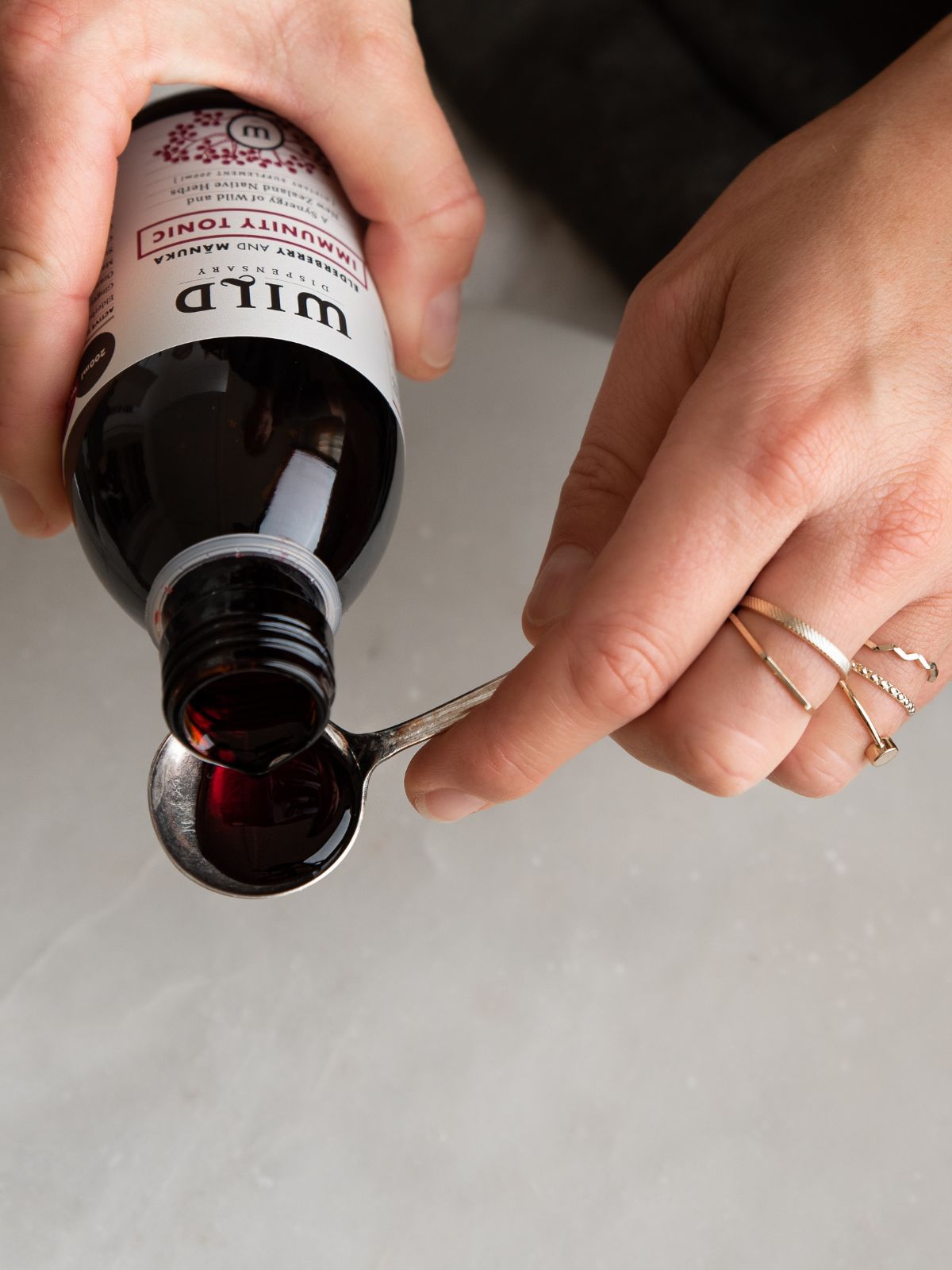 Deep red liquid Immunity Tonic being poured into small metal measuring spoon.