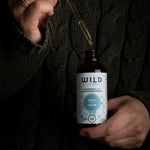 A person in a dark cable-knit sweater holds a bottle of 'Rest and Calm' with a glass dropper above the bottle.
