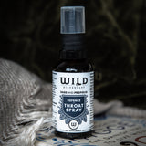 A bottle of Wild Dispensary Defence Throat Spray shown on a patterned surface with a textured grey blanket in the foreground and a dark, atmospheric background.