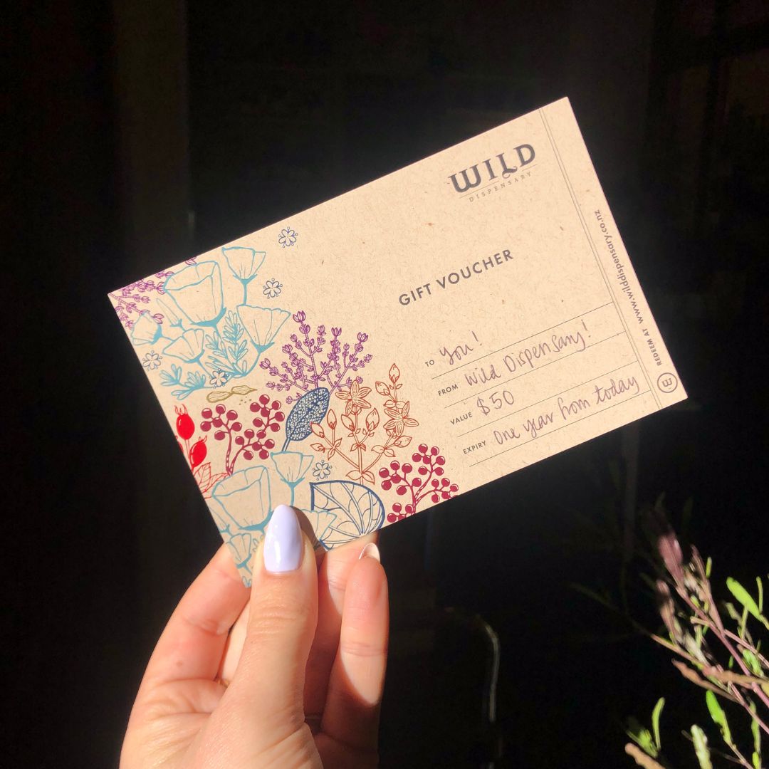 Hand holding a Wild Dispensary gift voucher with floral design on a dark background.